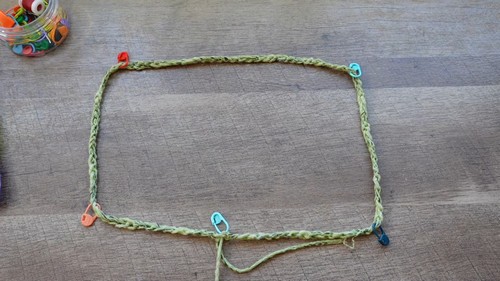 Foundation chain rectangle in sage green yarn on a wooden surface, marked with colorful stitch markers at the corners 