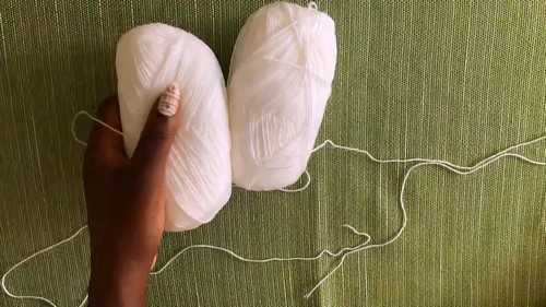 Two skeins of white yarn held in a hand against a green fabric background, used for a crochet maxi beach kimono