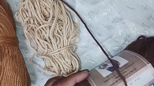  A skein of tan yarn and a ball of orange yarn resting beside a yarn label