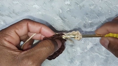 Hands crocheting a chain in dark brown yarn with a gold hook 