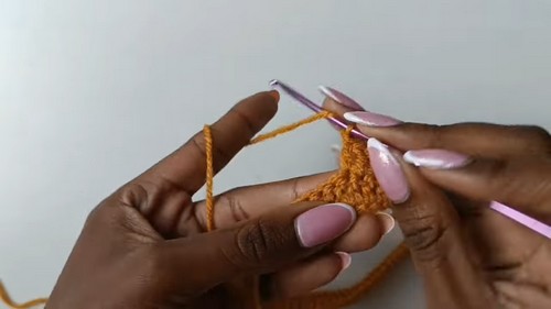 Hands beginning a mustard yellow crochet foundation chain with a pink hook 