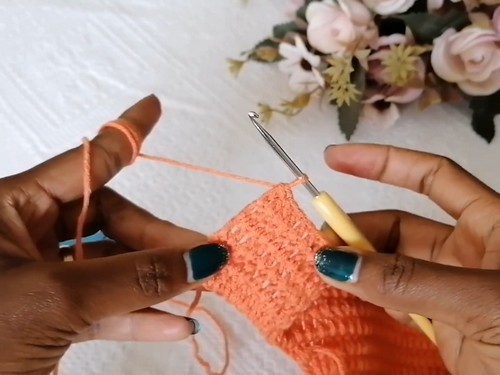 Hands working a row of single crochet across the orange fabric with a yellow hook 