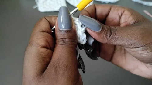 Close-up of hands crocheting a white granny square with a yellow hook 