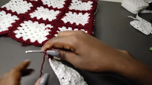 Hands joining granny squares together with dark red yarn and a grey hook 