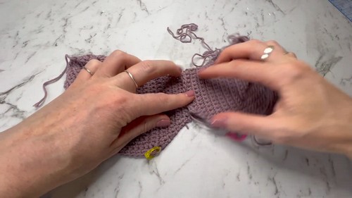 Hands holding a nearly finished mauve crochet crop top bralette, showing the shaped cup panels and underband construction 