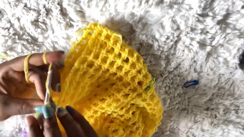 Hands working the yellow mesh crochet body panel, showing the square grid stitch in progress on a white fur surface
