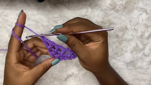 Hands beginning a purple crochet mesh stitch row from a foundation chain with a silver hook
