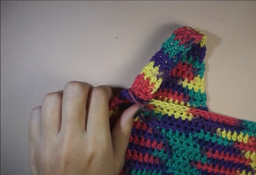 Hands folding the pointed V-neck edge of the rainbow crochet tank to check the shaping 