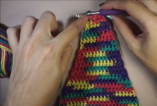 Hands working single crochet rows up the multicolor panel with a purple hook 