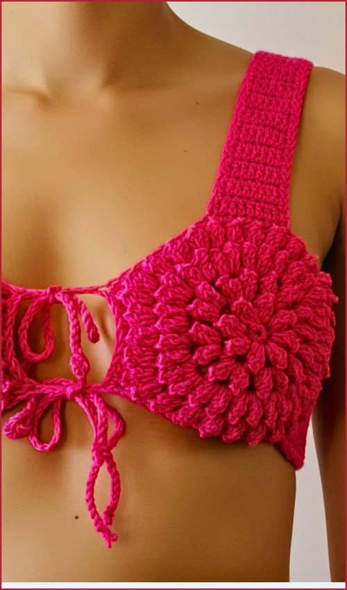 Close-up of hot pink crochet bikini top showing one puff stitch flower cup and front tie detail, worn on a mannequin 