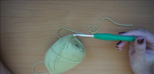 A ball of light green yarn with a green-handled hook resting on a wooden table