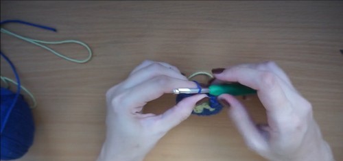 Hands joining a small navy and green granny square with a green hook 