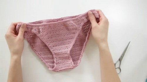 Holding a finished pink crochet bikini bottom before trimming yarn ends