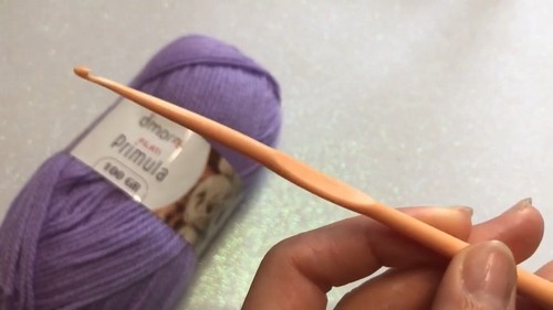 Peach crochet hook held alongside a ball of purple Dmora Primula yarn 