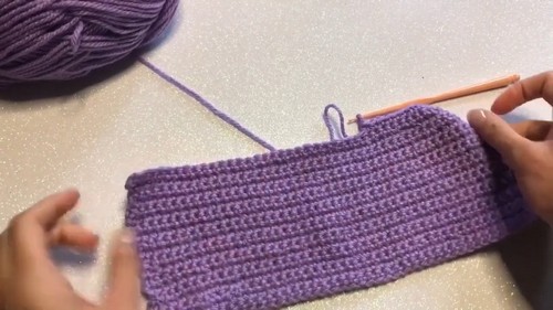 Hands crocheting a purple yarn panel in single crochet stitch, work in progress on a table with yarn ball
