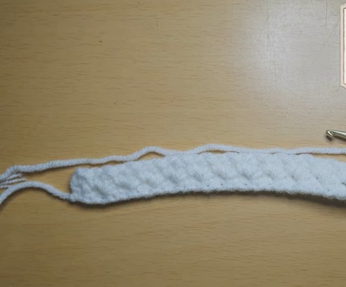 Close-up of the Suzette stitch texture in white cotton yarn, showing the alternating single crochet and double crochet pattern creating a diagonal bumpy texture.