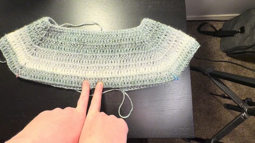 Flat lay of a finished crochet summer top showing raglan shaping, open armholes, and peplum ruffle hem in lightweight yarn