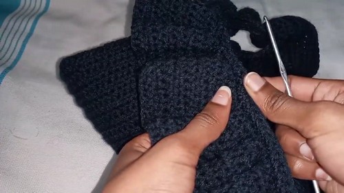 Image 2 — Hands using a metal crochet hook to join seams on a dark navy crochet fabric panel, shown close up on a light surface. 