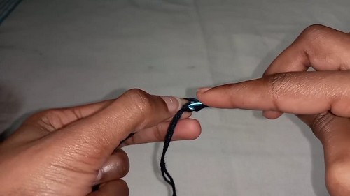 Hands forming a beginning slip knot with dark navy yarn and a thin crochet hook against a white surface