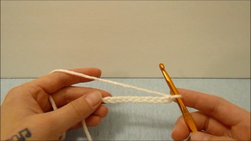 Hands holding a foundation chain of cream yarn with a gold crochet hook at the start of the project