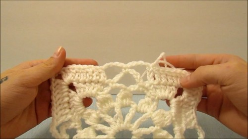 Hands holding a section of joined cream crochet floral medallion squares, showing the open petal structure and join points