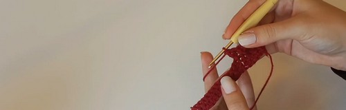 Hand holding a gold crochet hook with the first few stitches of a red yarn foundation chain 