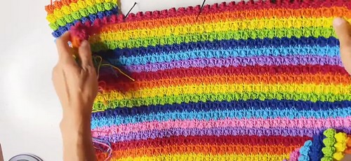 The rainbow striped crochet top laid flat, showing the full horizontal color stripe layout with popcorn stitch rows throughout and shaped armhole openings.