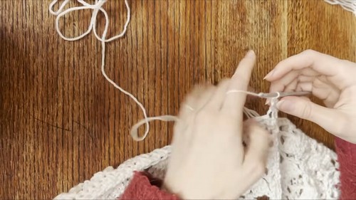 Hands joining two cream lace crochet panels on a wooden surface with white yarn