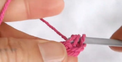 Hands forming early chain stitches with hot pink yarn and a metal crochet hook against a white background.