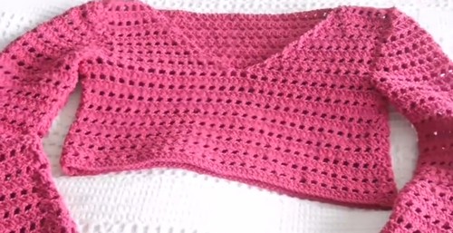 The finished pink crochet pullover laid flat showing the full construction — V-neckline, short cropped body, long sleeves with ribbed cuffs, and alternating solid and lace-stripe stitch bands.