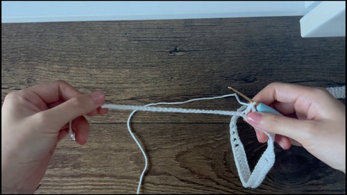 Hands working a white foundation chain with a blue hook. 