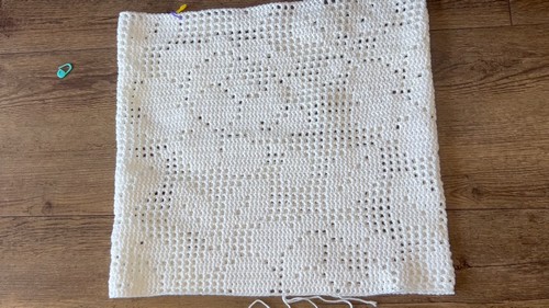 Top laid flat on a wood surface — full rectangular filet panel visible, rose chart clearly legible in the fabric. Stitch markers at corner. 