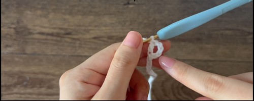 Close-up of hands forming an early chain stitch with white yarn and blue hook. 