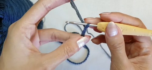 Hands working a foundation chain ring with navy yarn and a bamboo hook at the start of the construction