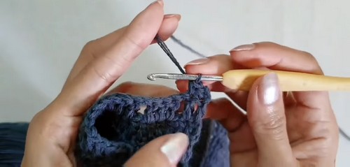 Close-up of hands working navy yarn with a bamboo crochet hook into the dense body of the shorts