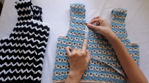 Flat lay of two finished crochet tank tops side by side, one in black and white and one in blue and cream, being joined at the shoulder with a crochet hook 