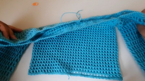 Flat lay of a teal crochet crop top body panel held open by hands, showing the even stitch texture across the width 