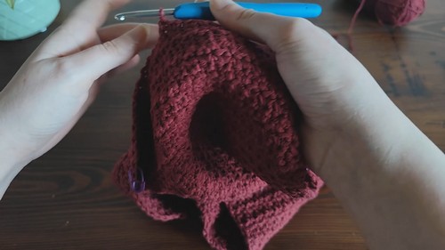Hands holding a partially completed burgundy crochet wrap top piece with armhole shaping visible and consistent star stitch texture throughout 