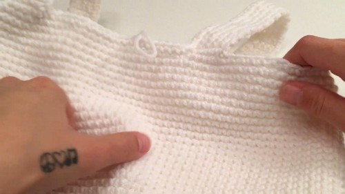 The finished white crochet tank top laid flat and held by hands, showing the dense upper section and the full alternating stitch-band construction. 