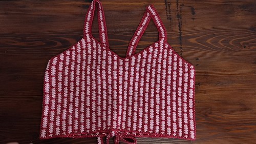 Flat lay of a completed two-color vertical brick pattern crochet top on a wooden surface showing spaghetti straps and front tie detail