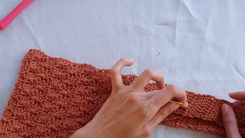 Hands crocheting shell stitch rows on a rust brown crochet top panel 