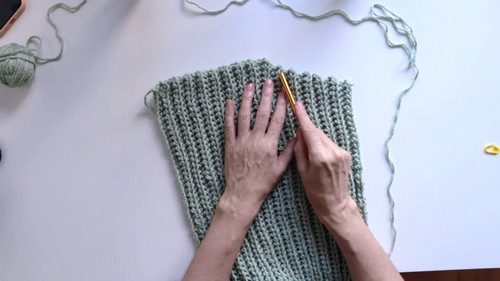 Hands smoothing a finished crochet panel flat on a table with a gold hook resting on top