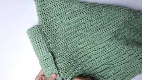 Hand holding up a completed crochet vest panel showing the ribbed body and armhole shaping