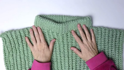 Hands spreading the assembled crochet vest flat showing the neckline and shoulder seam join
