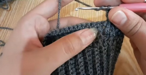 Hands working grey crochet ribbing rows with a silver hook, showing the vertical column texture of front post stitches