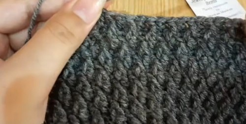 Hands crocheting a dense grey textured panel with a silver hook showing the pebbled body stitch in progress