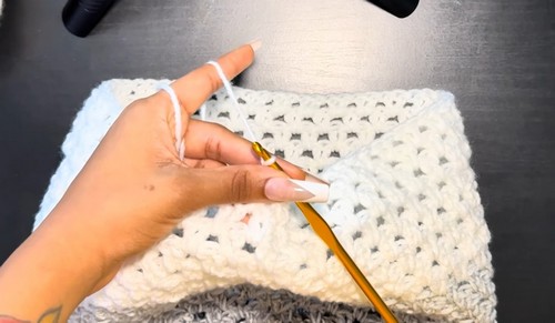 White section of the crochet sweater panel laid flat showing the open granny stitch clusters and corner shaping.