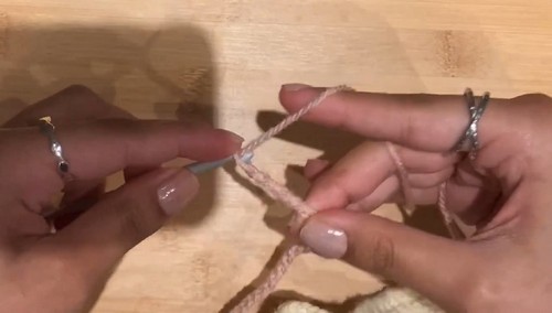 Foundation chain being started in pale pink yarn on a wooden surface with a small hook