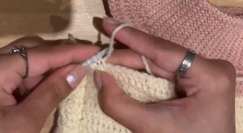 Cream HDC crochet fabric being worked at the neckline join with a small white hook
