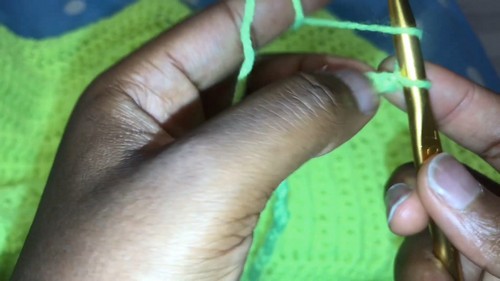 Close up of hands pulling neon green yarn through loops on a gold crochet hook.